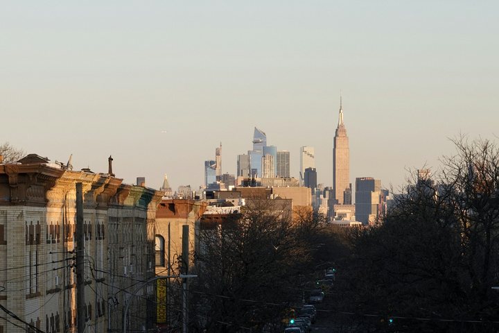 Brooklyn'de ağaçlı bir sokaktan görünen Manhattan silueti